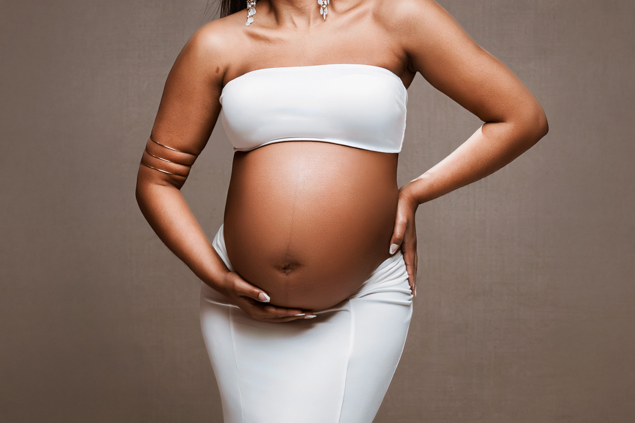 Close-up maternity portrait of an expecting mother cradling her baby bump in a white outfit